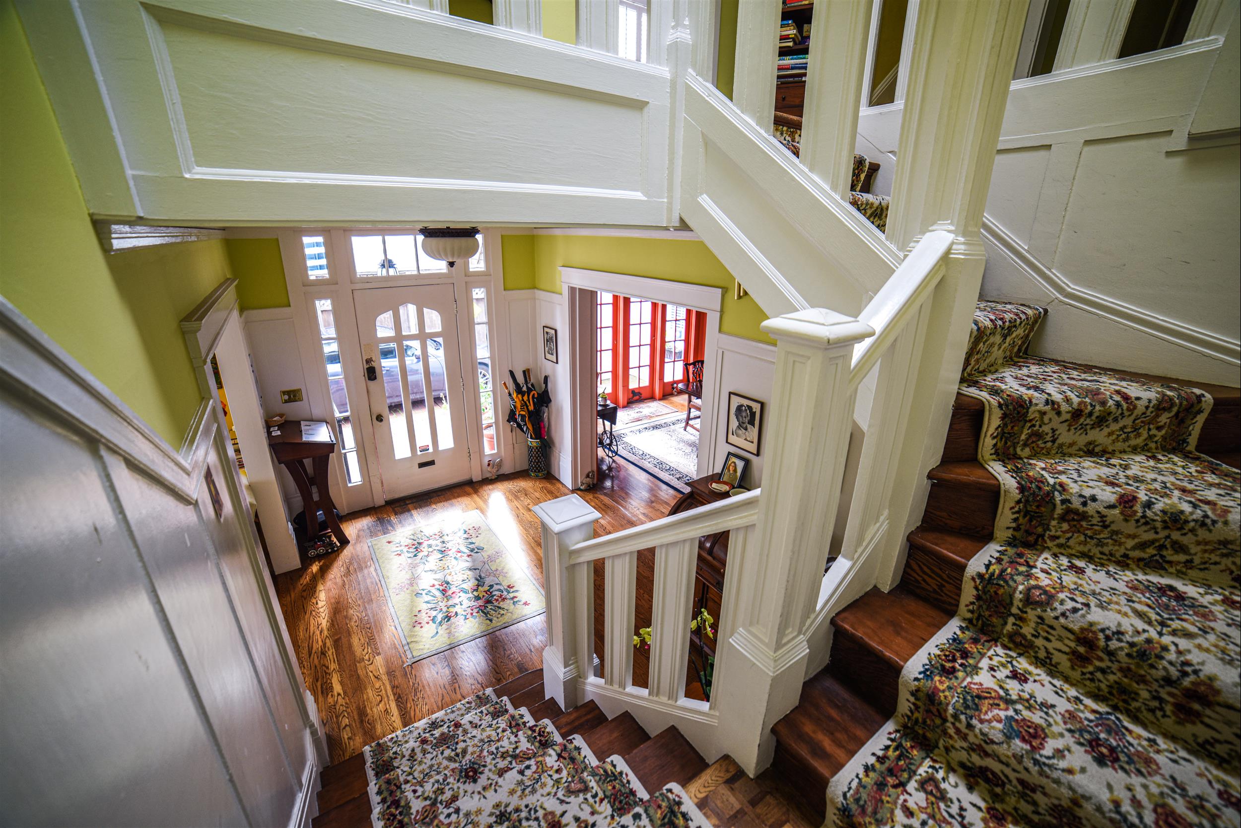 A staircase with white railings and floral carpet in a lobby with yellow walls and wooden flooring.